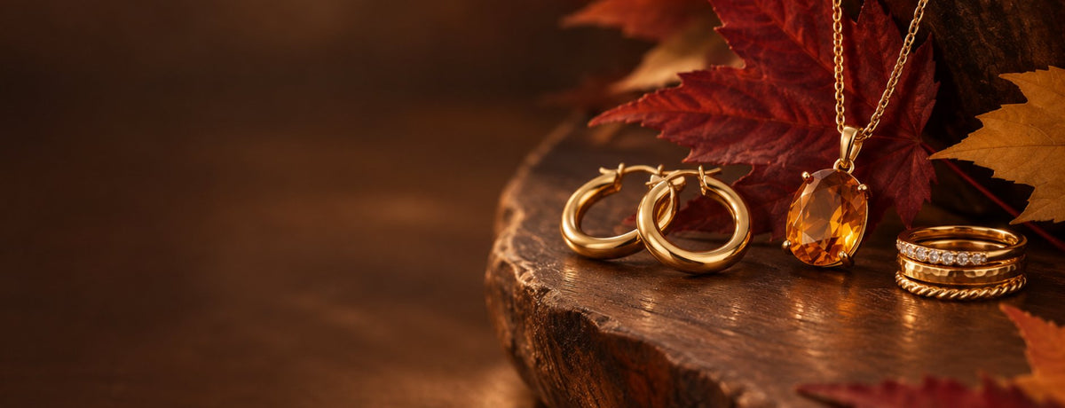 14k gold necklace with citrine pendant, gold hoop earrings and stacked gold rings on walnut with autumn maple leaves